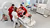 Flere helsearbeidere rundt en pasient på en båre ved en CT-skanner i et klinisk rom.