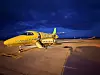 Et gult spesialfly står parkert på en rullebane ved solnedgang eller i skumring.