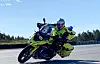 Gul ambulansemotorsykkel med fører i hjelm og reflekskjøretøy kjører på asfaltvei.
