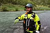 En redningsarbeider i gul jakke står i vannkanten ved en elv.