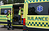 To personer i refleksvester står ved en åpen gulgrønn dansDe ambulanse med blått nød-symbol.