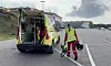 En gul ambulanse står med bakdørene åpne, mens to personer i refleksklær går ved siden av med utstyr.