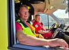 To menn i rød uniform og refleksvest sitter foran i en ambulanse.