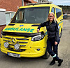 En gul Mercedes-ambulanse står parkert mens Ingvild Grønnerud står ved siden av foran.