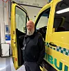 En mann står ved siden av en gul ambulanse med åpne dører inne i et lyst verksted.