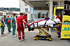 Personell i arbeidsklær triller en båre med pasient ved en ambulanse og sykehusinngang.