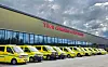 En rekke gule ambulanser står parkert foran et stort konferansesenter under en overskyet himmel.