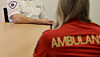 To personer sitter ved et bord; den nærmeste har rød ambulansejakke, den andre hvit uniform.