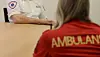 To personer sitter ved et bord; den nærmeste har rød ambulansejakke, den andre hvit uniform.