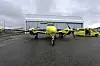 Gult tomotors fly står på våt asfalt foran en hangar, med flere gule luftfartøy i bakgrunnen.