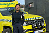 Uniformert ambulansearbeider står foran en gul ambulanse utenfor en bygning.