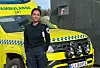 Uniformert ambulansearbeider står foran en gul ambulanse utenfor en bygning.